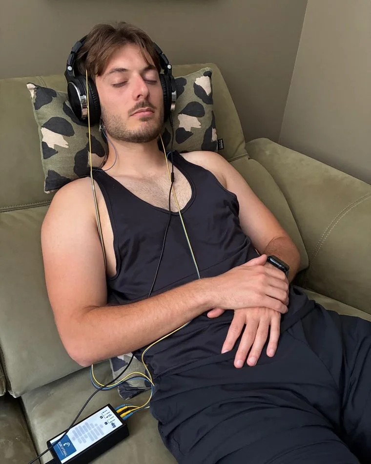 Jeune homme allongé les yeux fermés, casque sur les oreilles, le boîtier NeurOptimal® posé près de lui